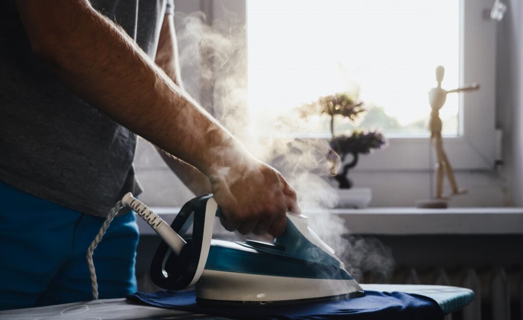A man using an iron to steam a shirt in front of a window.